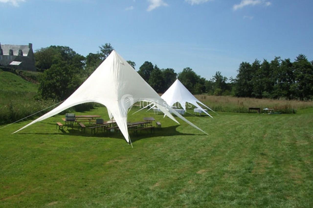Deux tentes blanches triangulaires installées sur une pelouse, entourées de tables et de bancs en plein air.