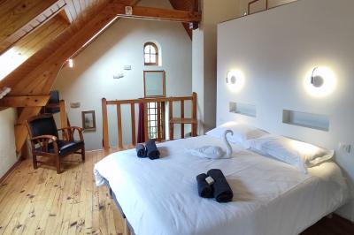 Chambre mansardée avec lit double, serviettes pliées, cygne en serviette, fauteuil et lumière naturelle.