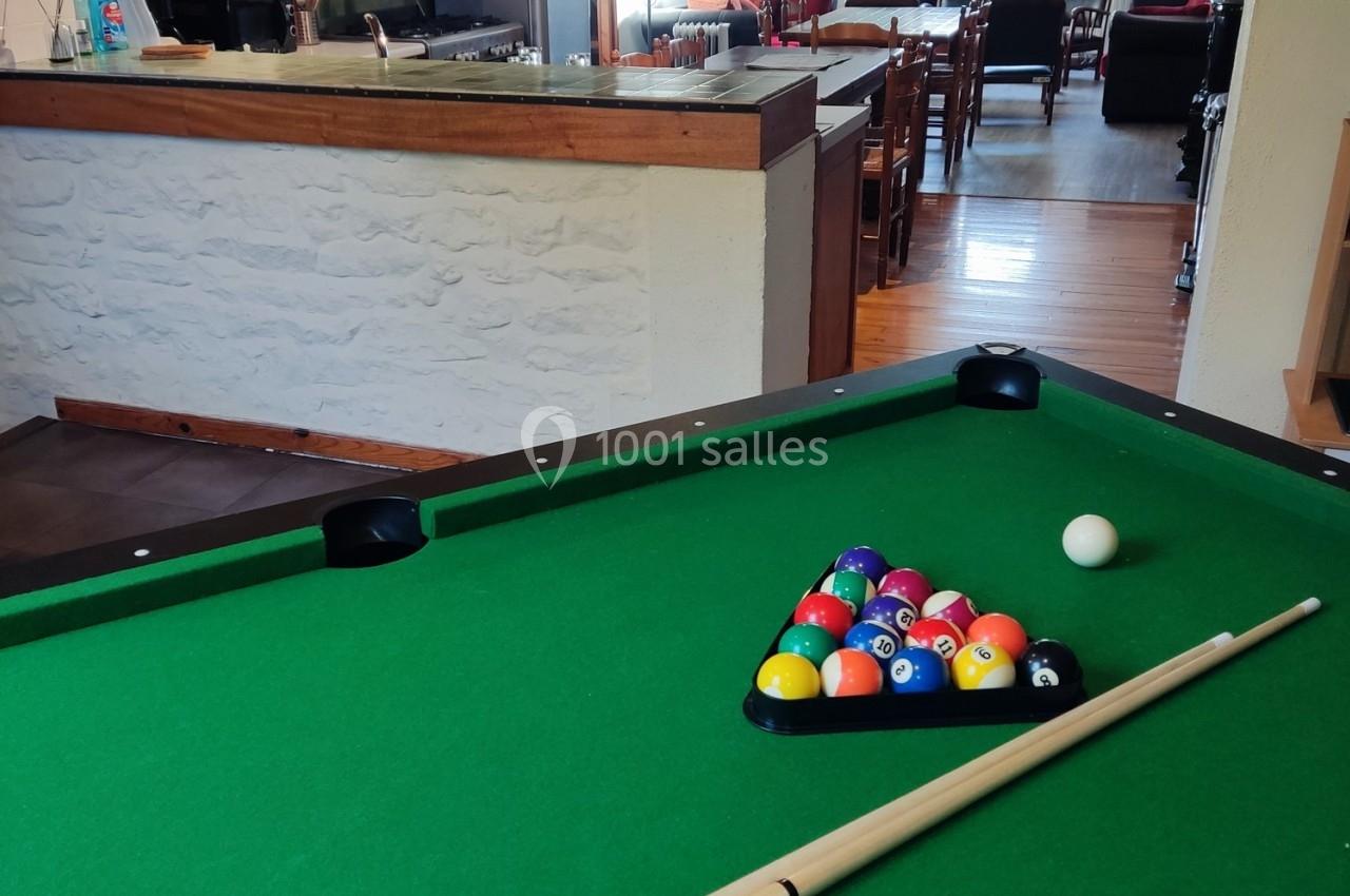 Table de billard avec des boules alignées en triangle, une queue de billard posée dessus et une pièce en arrière-plan.