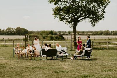 Table décorée avec des bougies, fleurs et sets en osier, entourée de coussins, bancs et éléments rustiques en bois.