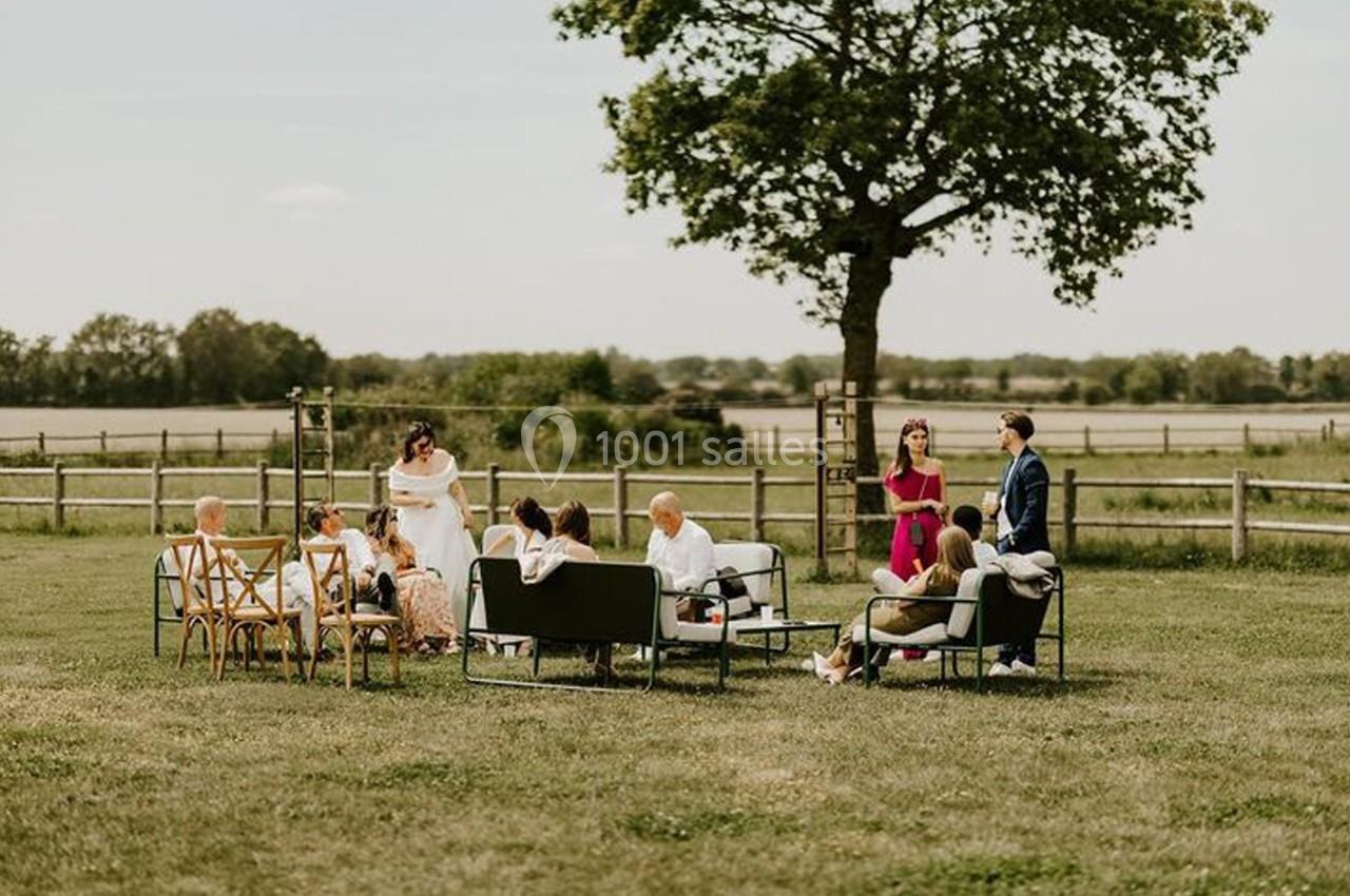 Groupe de personnes assises et discutant dans un champ, près d'un arbre et de clôtures en bois.