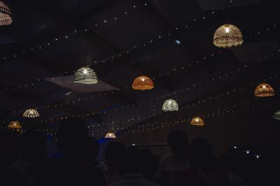 Table décorée avec des bougies, fleurs et sets en osier, entourée de coussins, bancs et éléments rustiques en bois.