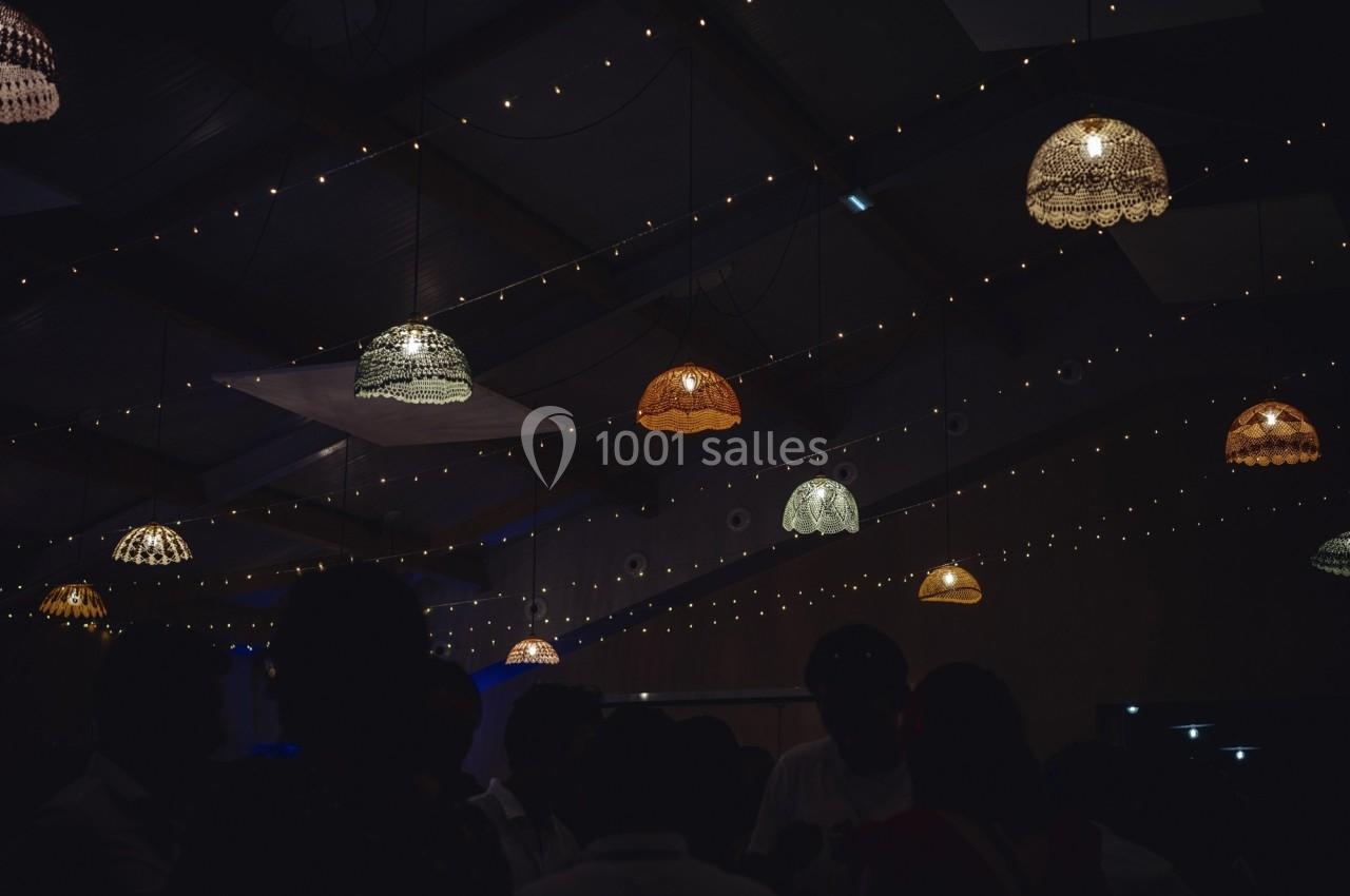 Des lampes suspendues éclairent faiblement une salle sombre décorée de guirlandes lumineuses.