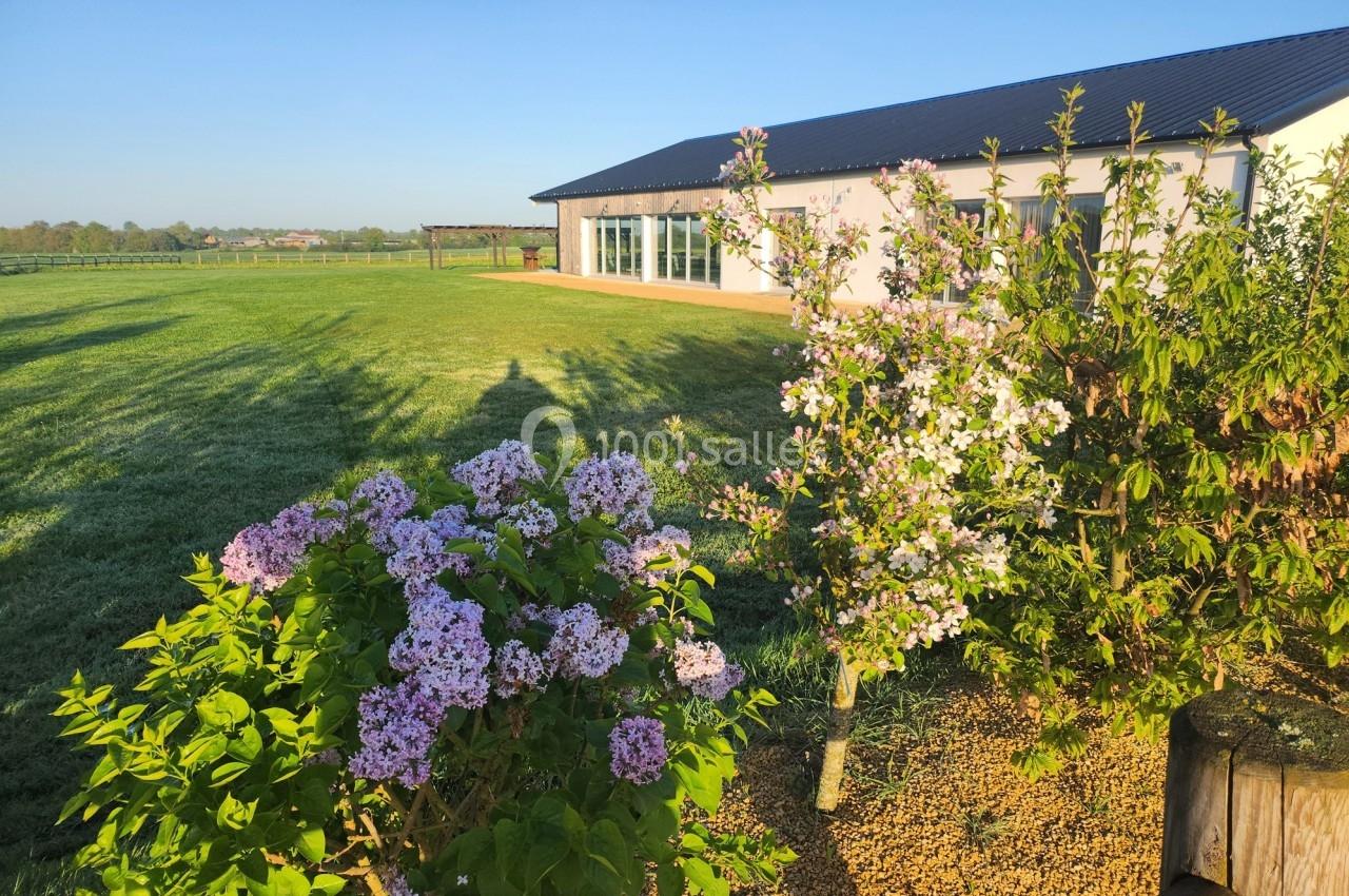 Bâtiment moderne entouré d'un grand jardin verdoyant avec des arbustes fleuris sous un ciel dégagé.