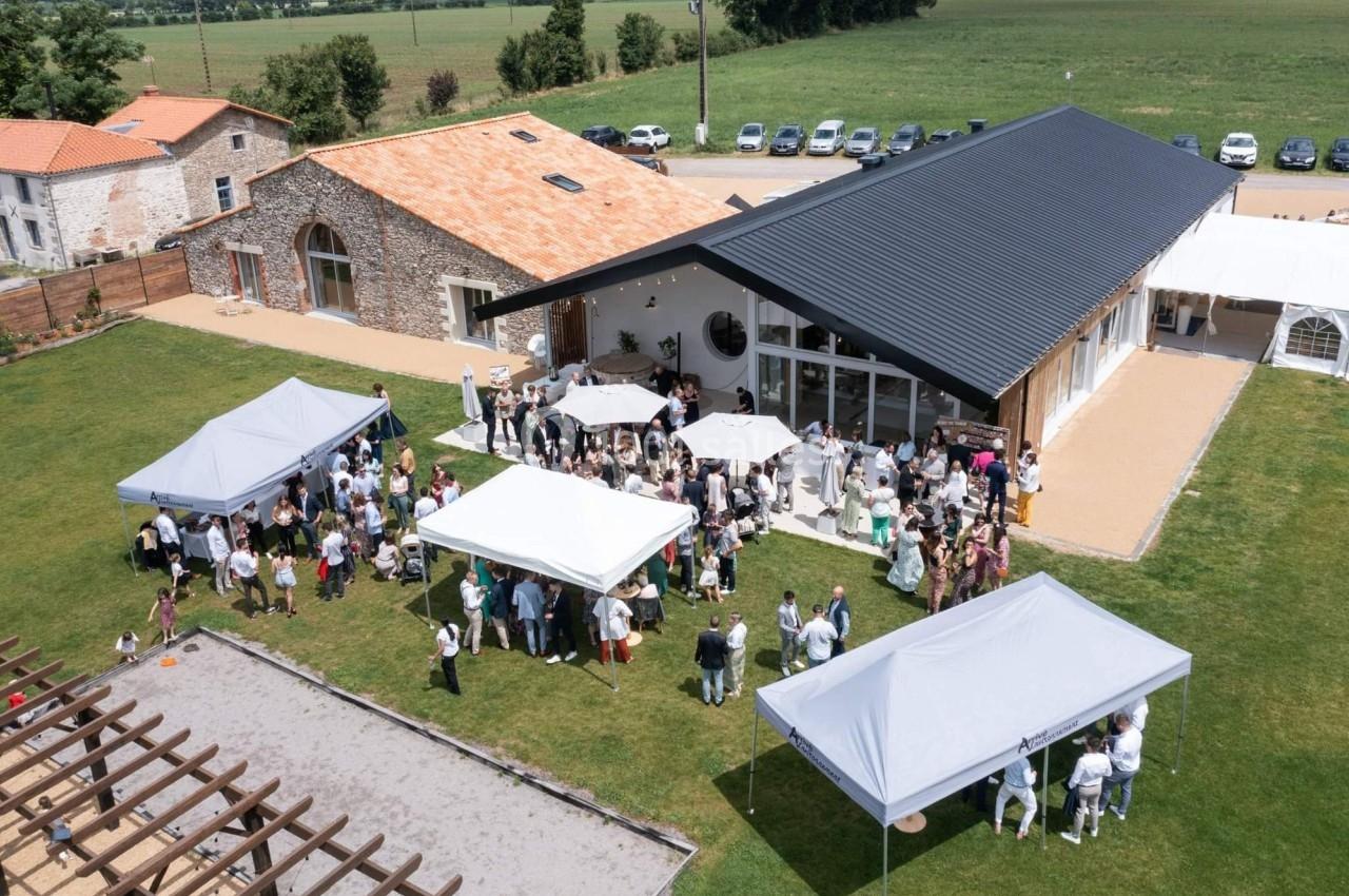 Vue aérienne d'une réception en extérieur avec des invités rassemblés sous des tonnelles près d'un bâtiment moderne.