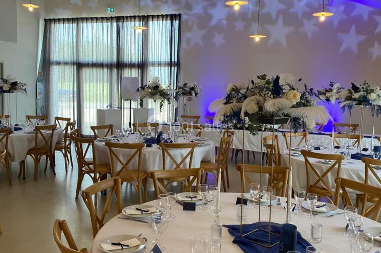 Salle de réception décorée avec des tables rondes, nappes blanches, chaises en bois et arrangements floraux élégants.