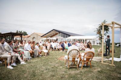 Table décorée avec des bougies, fleurs et sets en osier, entourée de coussins, bancs et éléments rustiques en bois.