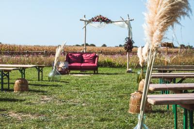 Table décorée avec des bougies, fleurs et sets en osier, entourée de coussins, bancs et éléments rustiques en bois.