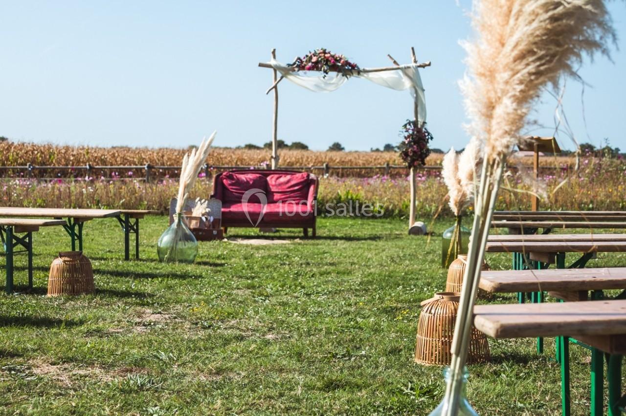 Décoration de mariage champêtre en extérieur avec arche fleurie, bancs en bois et herbes de la pampa.