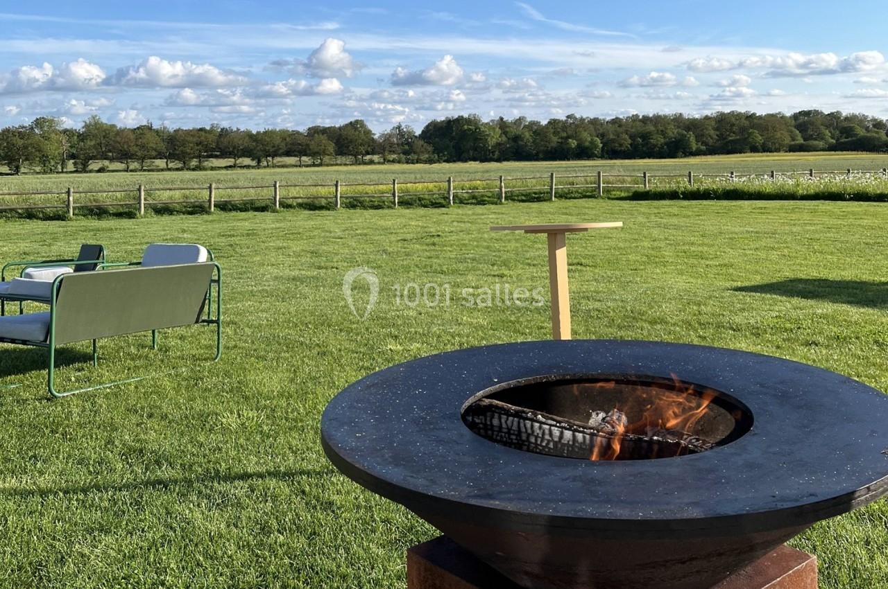 Brasero allumé dans un grand jardin verdoyant avec des sièges et une table en arrière-plan, sous un ciel dégagé.