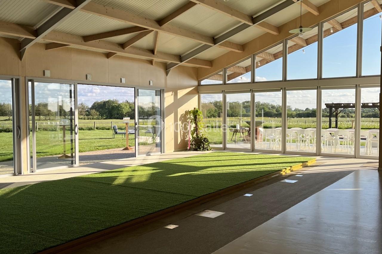 Salle lumineuse avec de grandes baies vitrées donnant sur un espace extérieur verdoyant et des chaises blanches alignées.