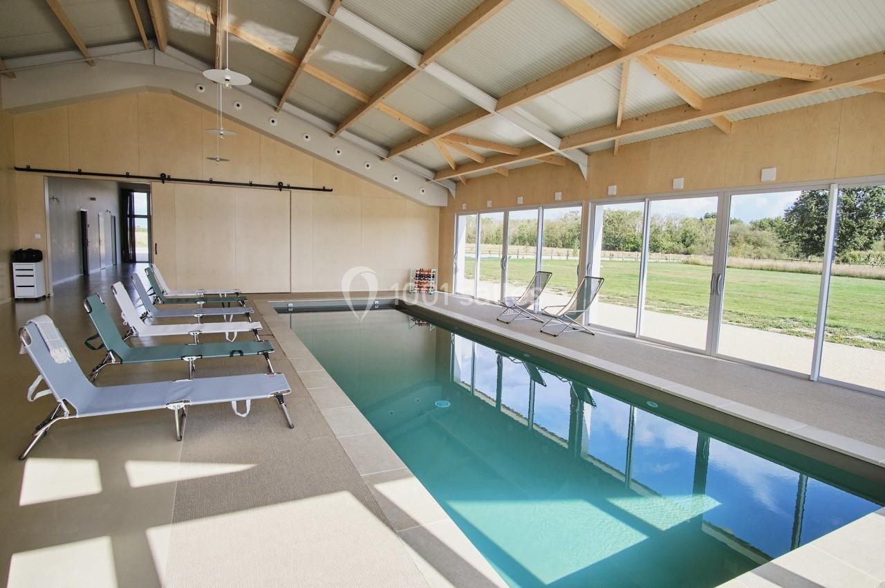 Piscine intérieure avec chaises longues, grandes baies vitrées donnant sur un jardin verdoyant.