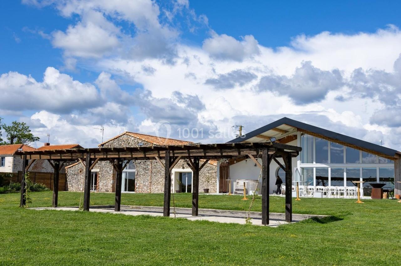 Bâtiments en pierre et structure en bois dans un espace vert sous un ciel partiellement nuageux.