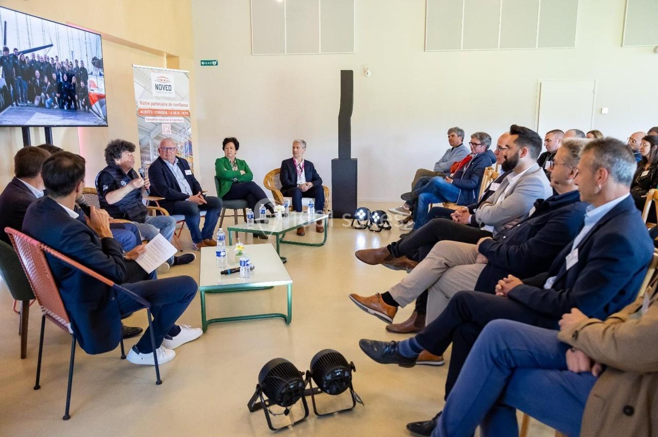 Un groupe de personnes assises en cercle participe à une discussion dans une salle lumineuse avec un écran en arrière-plan.