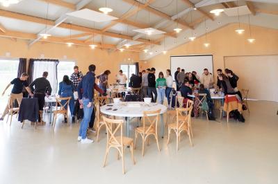 Des personnes participent à un atelier créatif dans une salle lumineuse, entourées de tables et de matériel artistique.