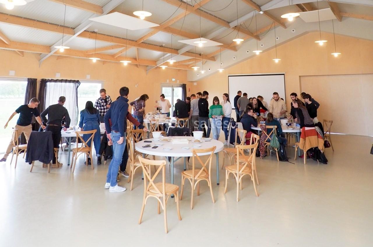 Des personnes discutent et travaillent en groupe autour de tables dans une grande salle lumineuse au style moderne.