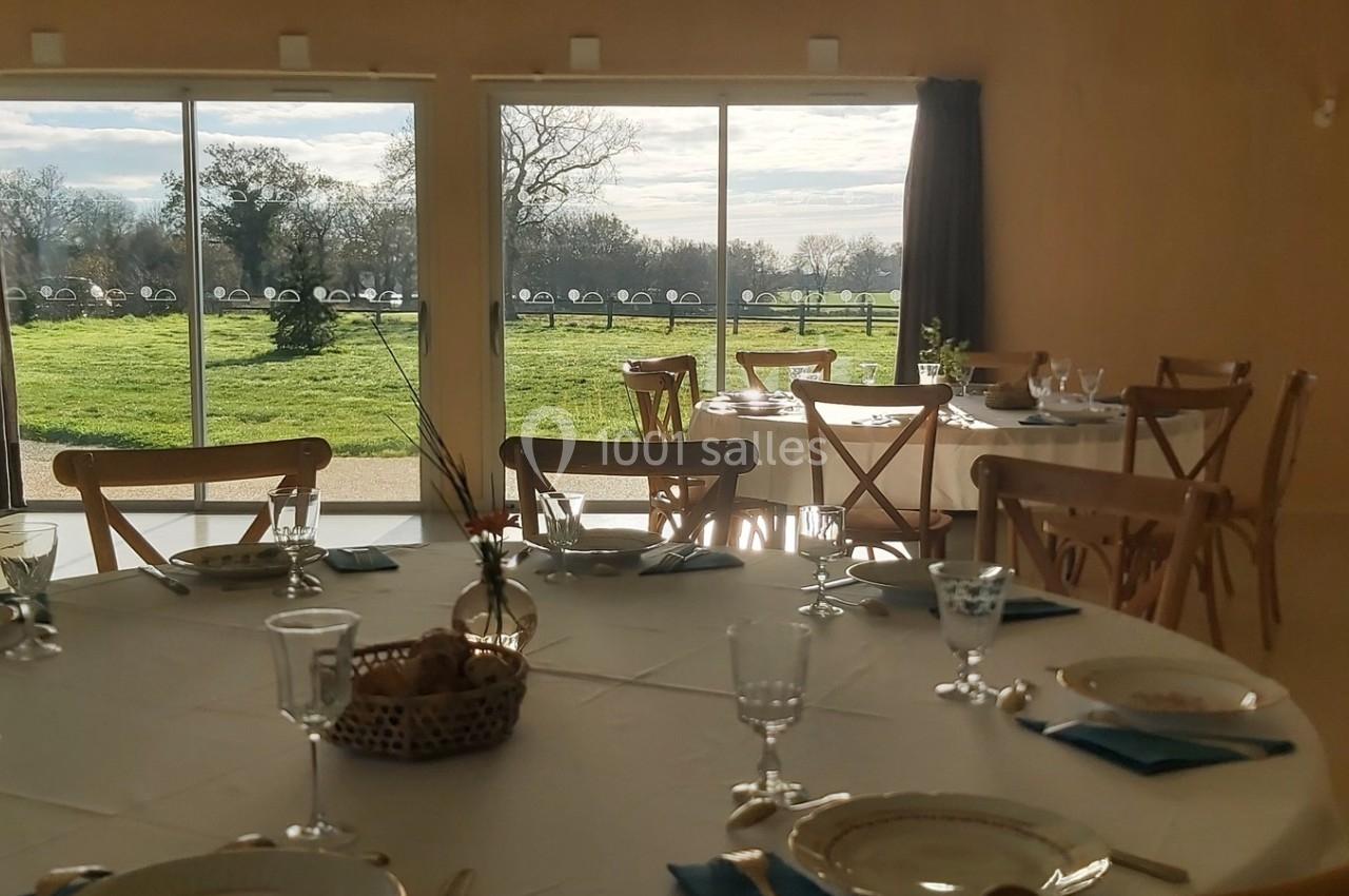 Salle lumineuse avec tables dressées, vue sur un jardin verdoyant à travers de grandes baies vitrées.