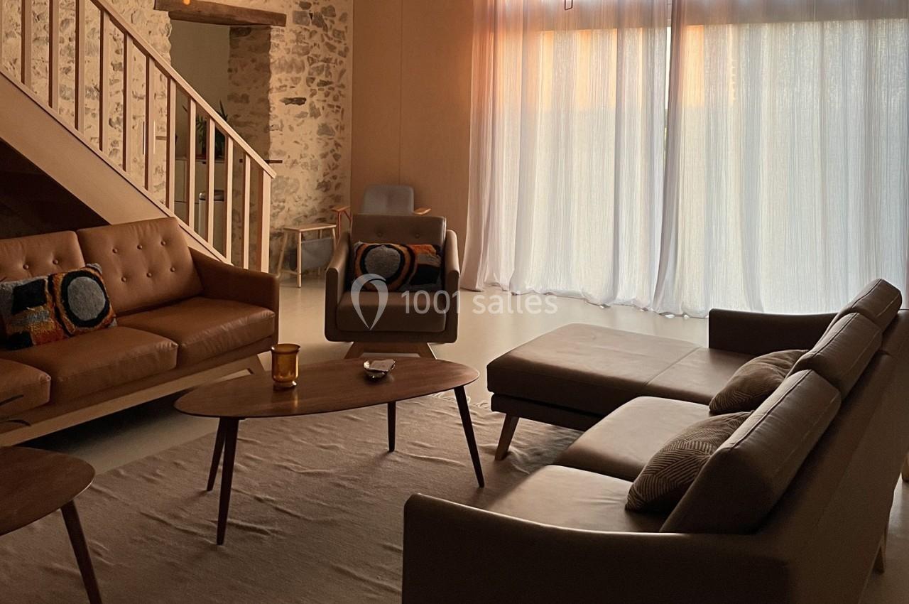 Salon chaleureux avec canapé en cuir, table basse en bois, tapis beige et lumière naturelle filtrée par des rideaux.