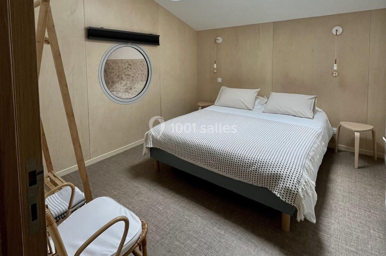 Chambre minimaliste avec lit double, murs en bois clair, hublot rond et mobilier en bois naturel.
