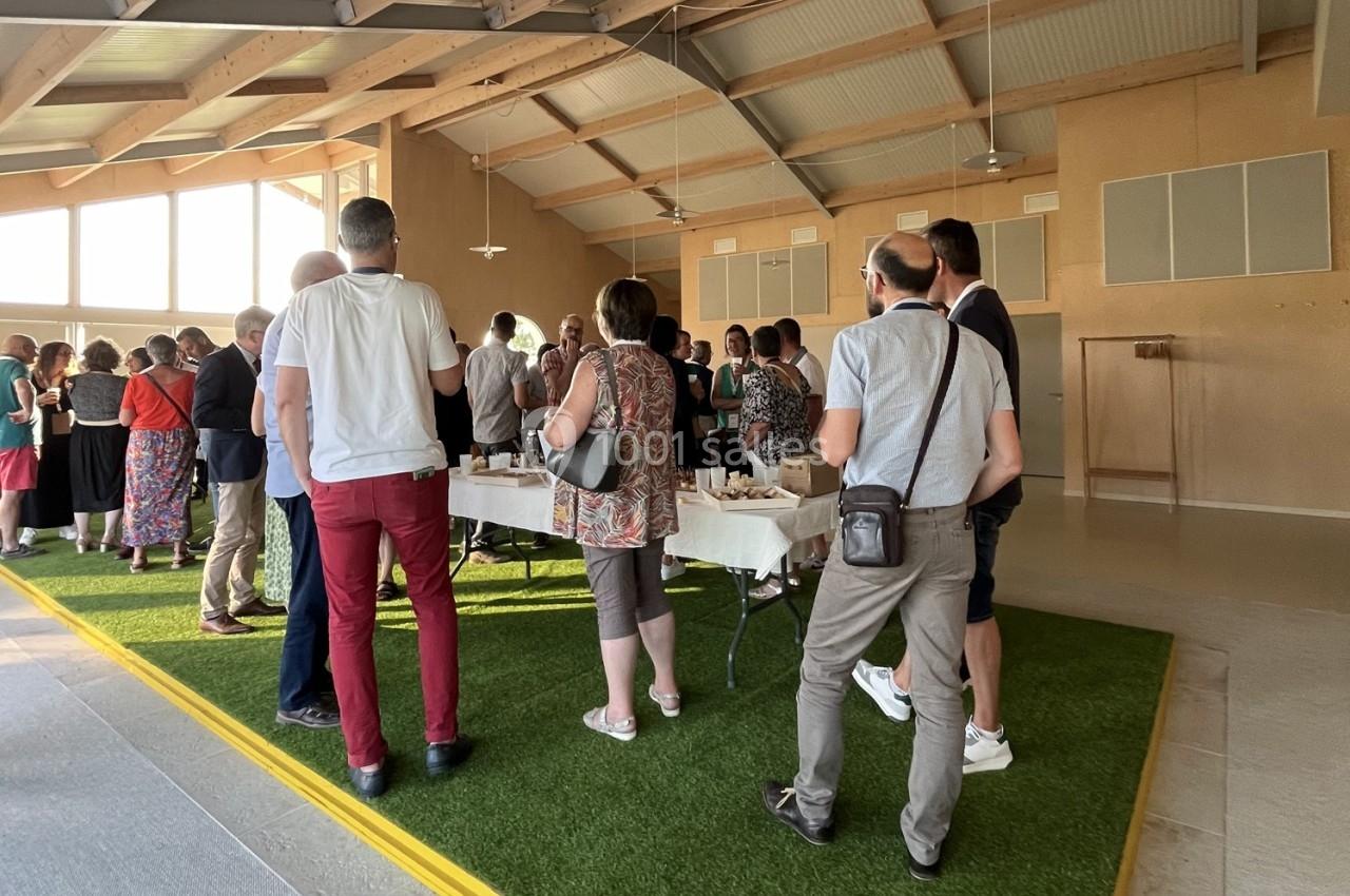 Groupe de personnes debout autour de tables lors d'un événement dans une salle lumineuse avec un sol partiellement recouvert…