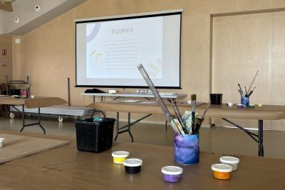 Des personnes participent à un atelier créatif dans une salle lumineuse, entourées de tables et de matériel artistique.