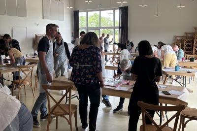 Des personnes participent à un atelier créatif dans une salle lumineuse, entourées de tables et de matériel artistique.