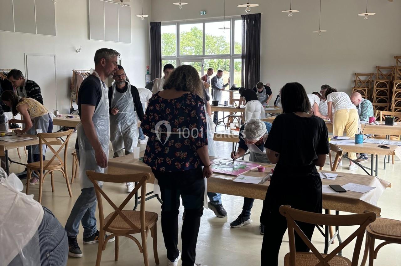 Des personnes participent à un atelier créatif dans une salle lumineuse, entourées de tables et de matériel artistique.