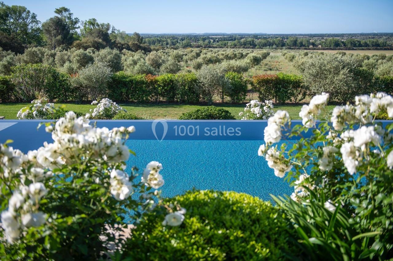 Vue d'une piscine entourée de fleurs blanches et de verdure, avec un paysage de campagne à l'arrière-plan.