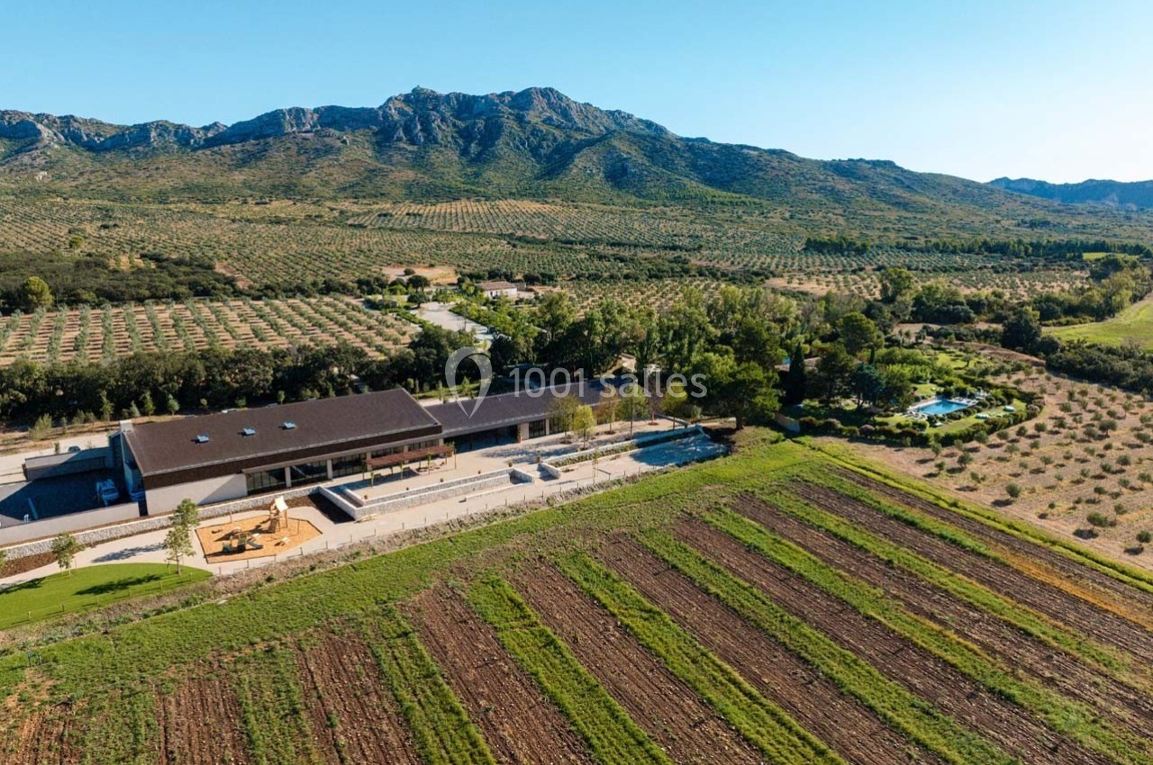 Vue aérienne d'un domaine agricole avec champs cultivés, bâtiment moderne et collines en arrière-plan.