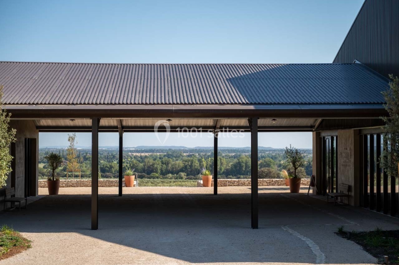 Vue d'un bâtiment moderne avec toit en métal, ouvert sur un paysage rural avec des collines et des arbres à l'horizon.