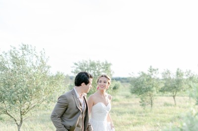 Un couple en tenue de mariage marche dans un champ verdoyant par une journée ensoleillée.