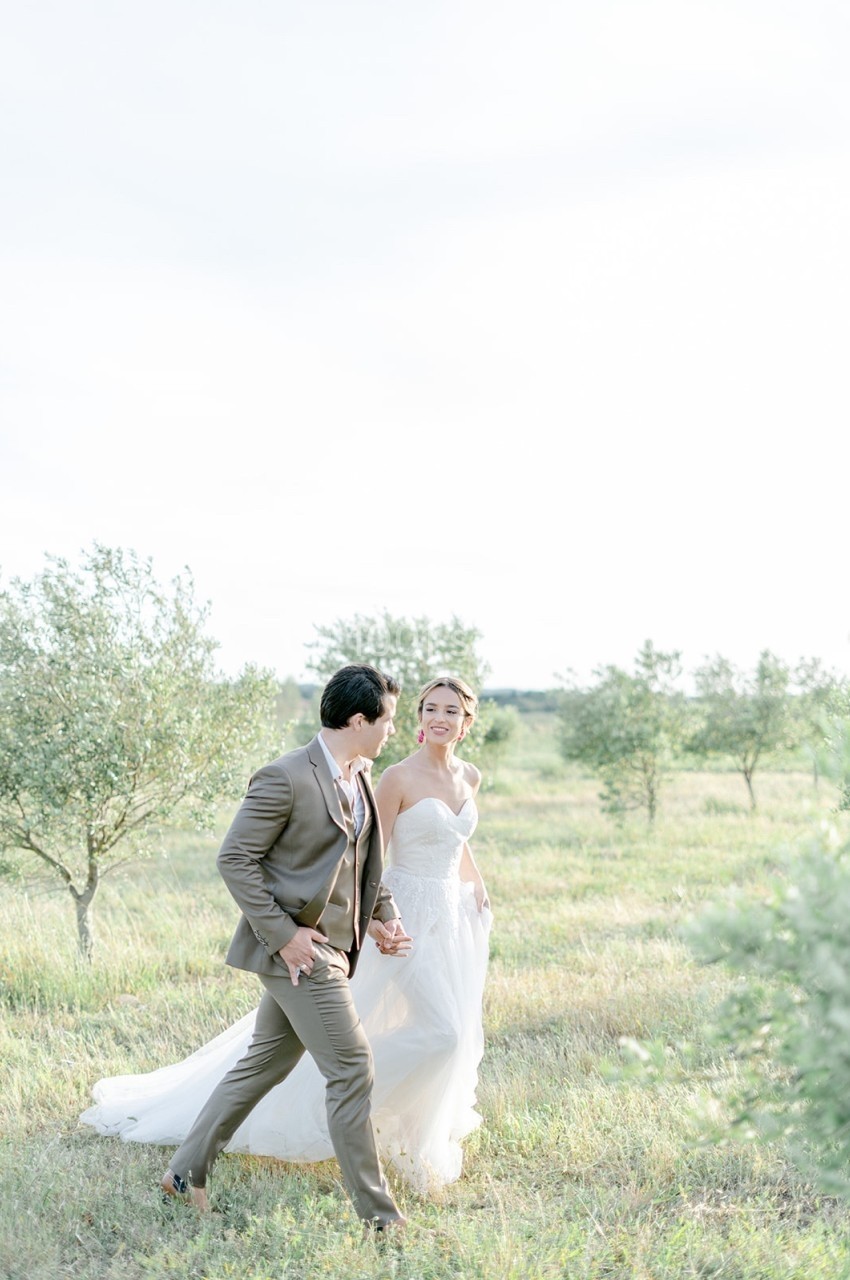 Un couple en tenue de mariage marche dans un champ verdoyant par une journée ensoleillée.