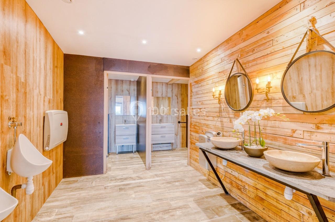 Salle de bain moderne avec murs en bois, vasques doubles, miroirs ronds et éclairage chaleureux.