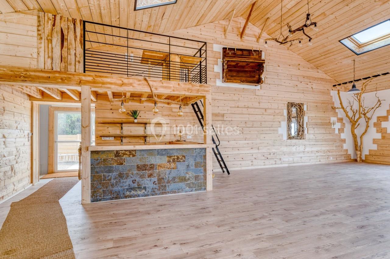 Intérieur spacieux en bois avec mezzanine, bar en pierre, parquet clair et puits de lumière.