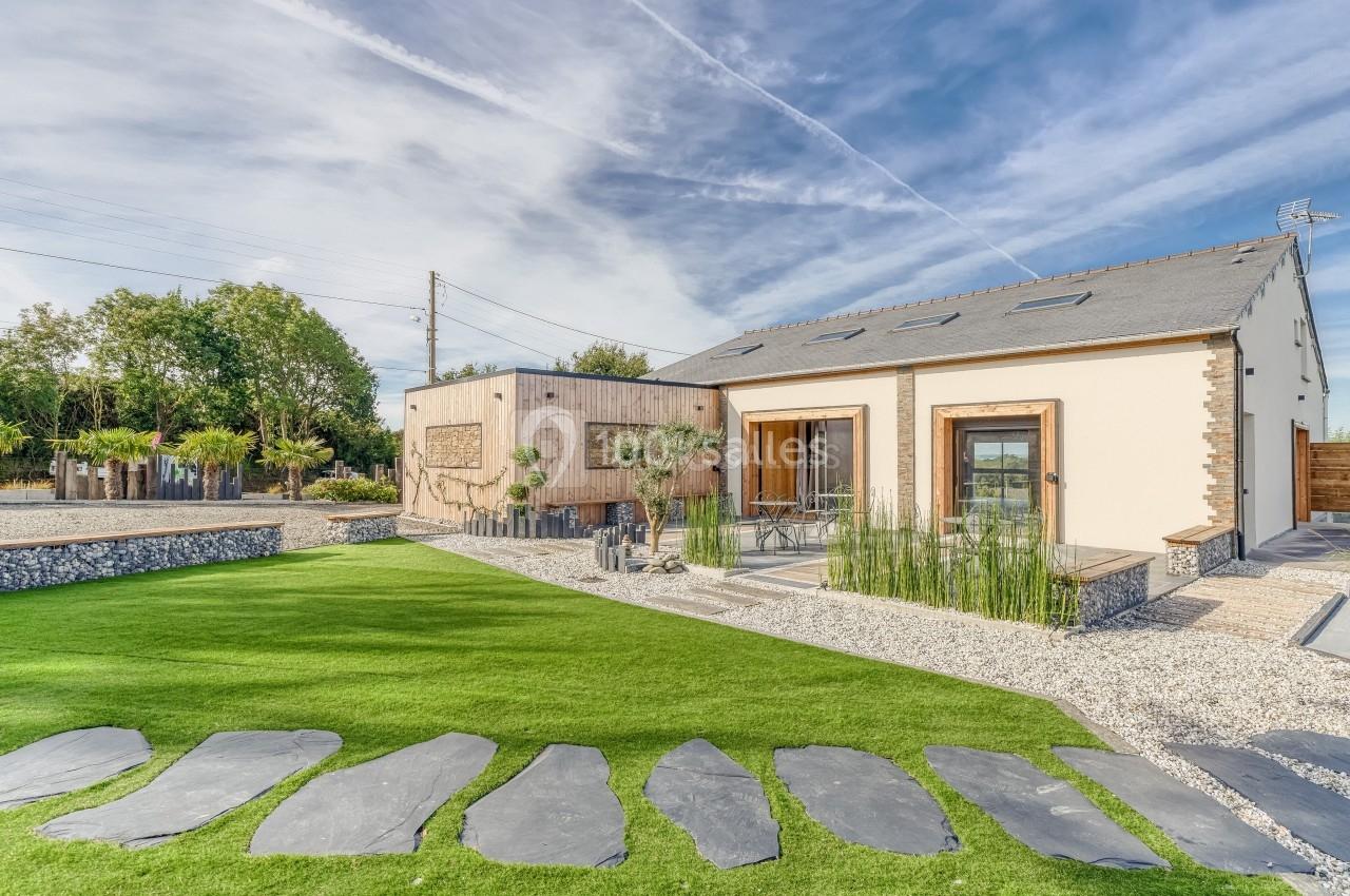 Maison moderne avec façade claire, terrasse en bois, jardin paysager et allée en dalles sur pelouse.