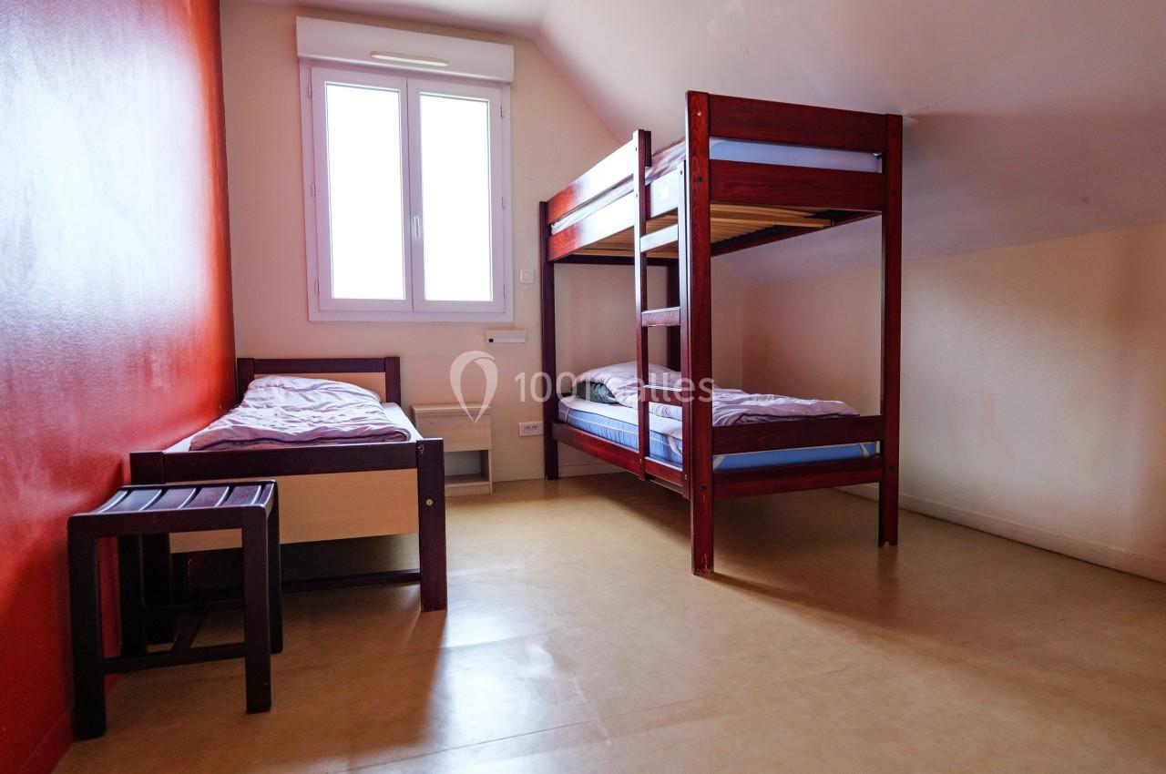 Chambre simple avec un lit simple, un lit superposé, un tabouret et une fenêtre laissant entrer la lumière naturelle.