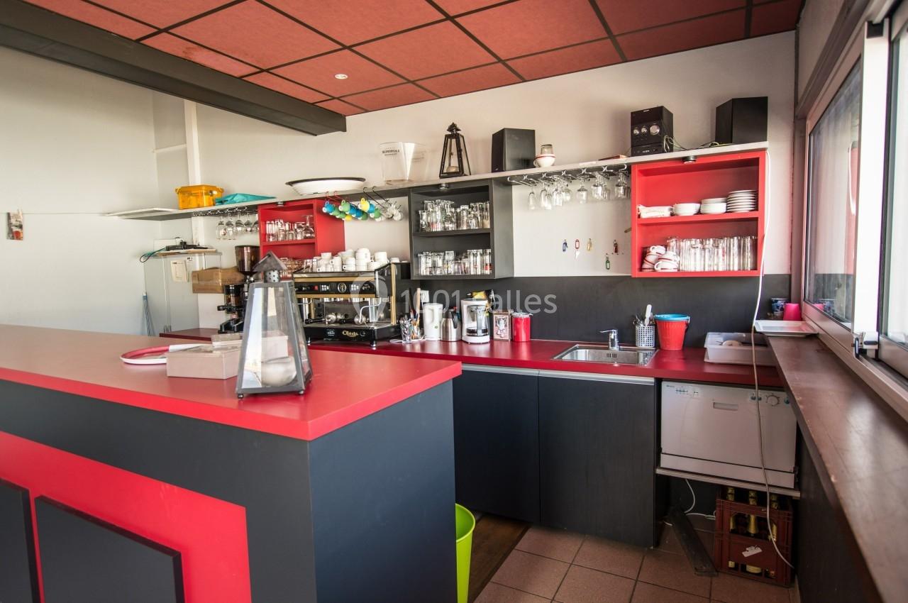 Cuisine équipée avec un comptoir rouge, étagères ouvertes contenant vaisselle et ustensiles, et un évier près d'une fenêtre.