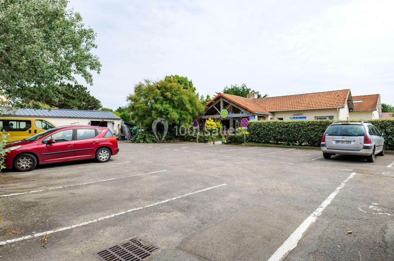 Parking extérieur avec quelques voitures stationnées devant un bâtiment à toit rouge entouré de végétation.