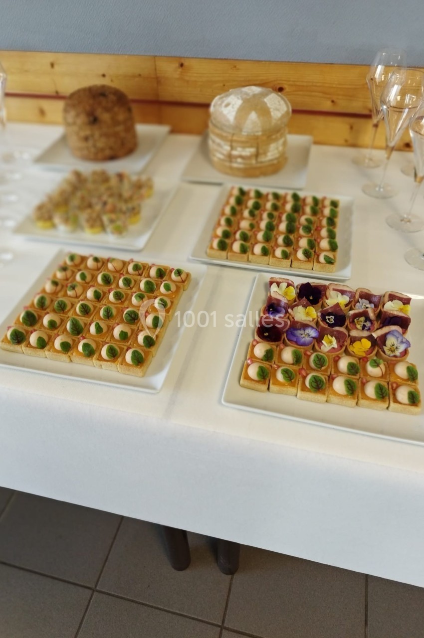 Plateau de canapés variés avec des fleurs comestibles, entouré de pains et de flûtes à champagne sur une table blanche.