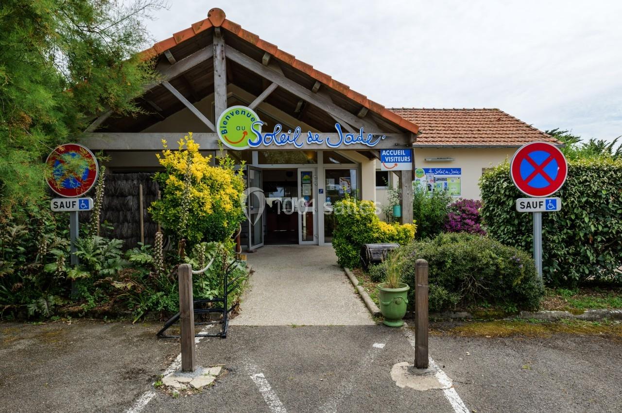 Entrée d'un bâtiment avec une enseigne ’Auberge du Soleil’, entourée de végétation et de panneaux de signalisation.