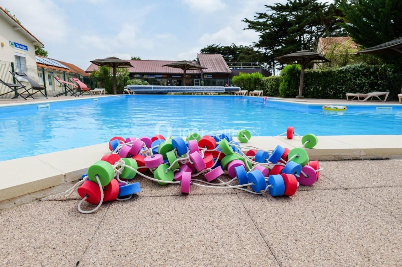 Flotteurs colorés posés au bord d'une piscine extérieure entourée de transats et de végétation.