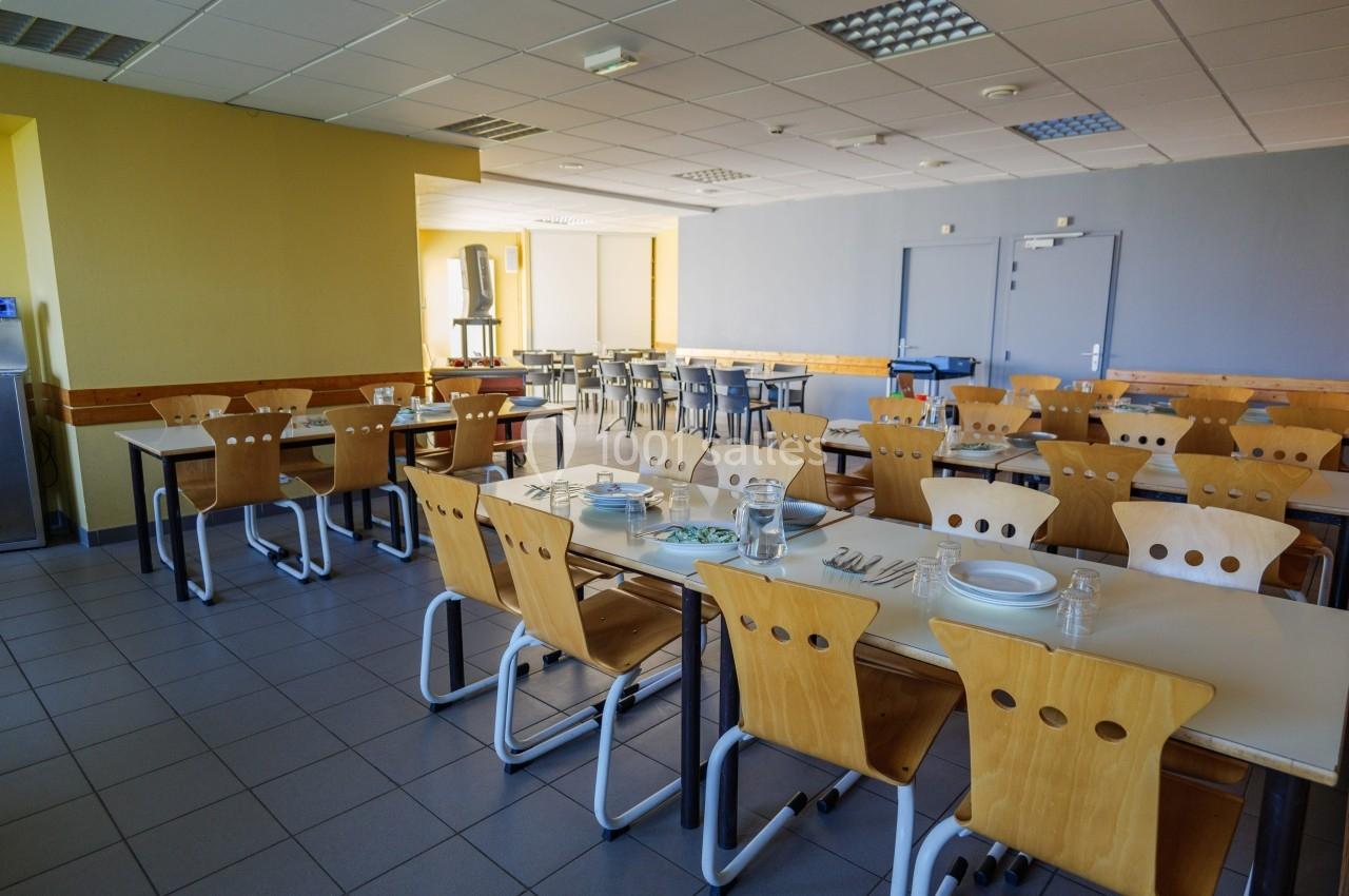 Salle de restauration avec tables dressées, chaises en bois clair et lumière naturelle entrant par les fenêtres.