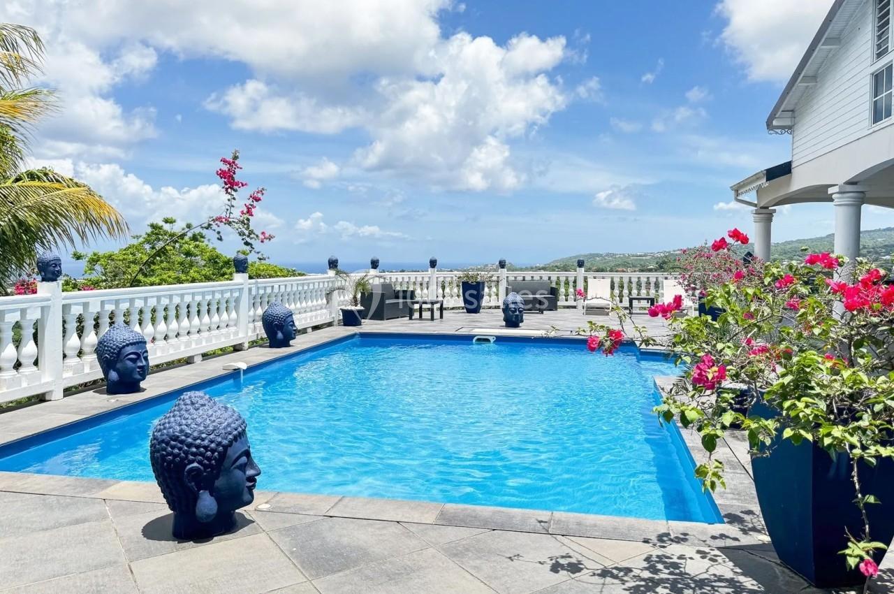 Piscine extérieure entourée de statues de têtes de Bouddha, fleurs tropicales et vue dégagée sur un paysage lointain.