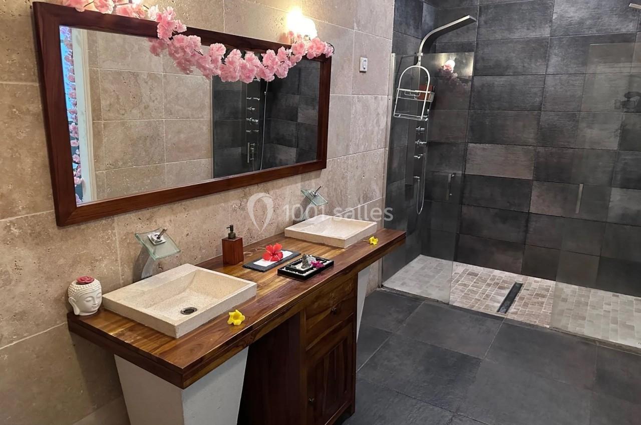 Salle de bain moderne avec double vasque en bois, grand miroir, douche à l'italienne et décoration florale.