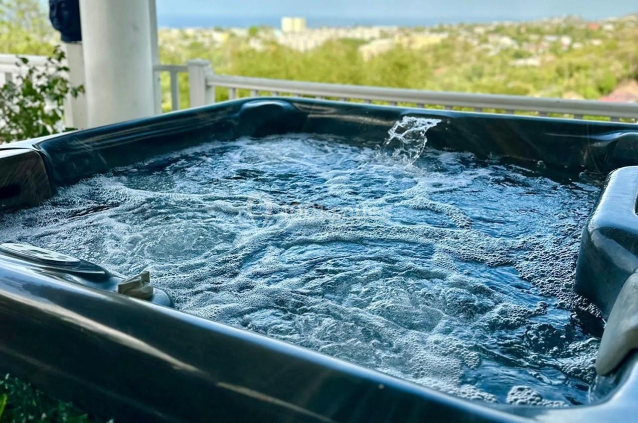 Vue rapprochée d'un jacuzzi en fonctionnement avec un paysage urbain et végétal en arrière-plan.