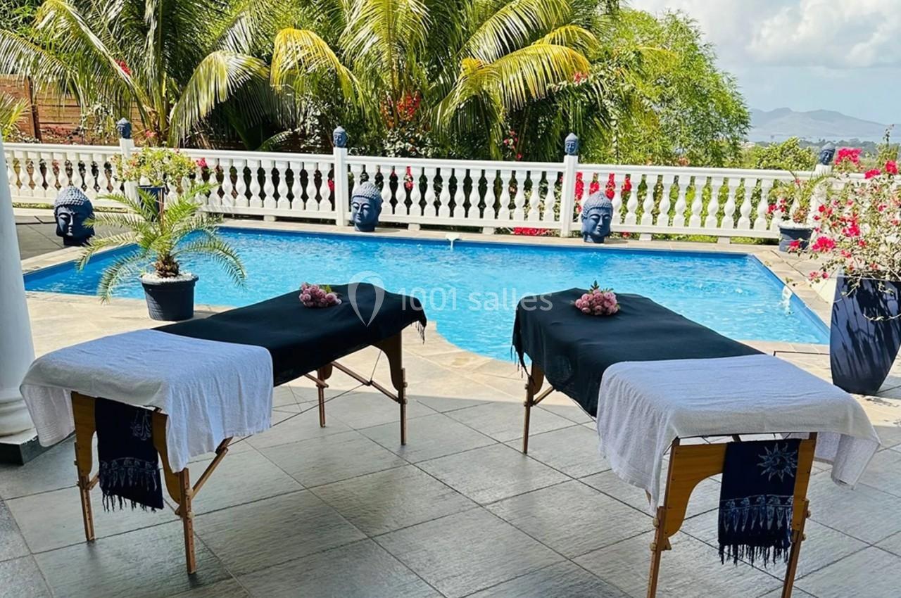 Deux tables de massage couvertes de draps, installées près d'une piscine entourée de végétation tropicale.