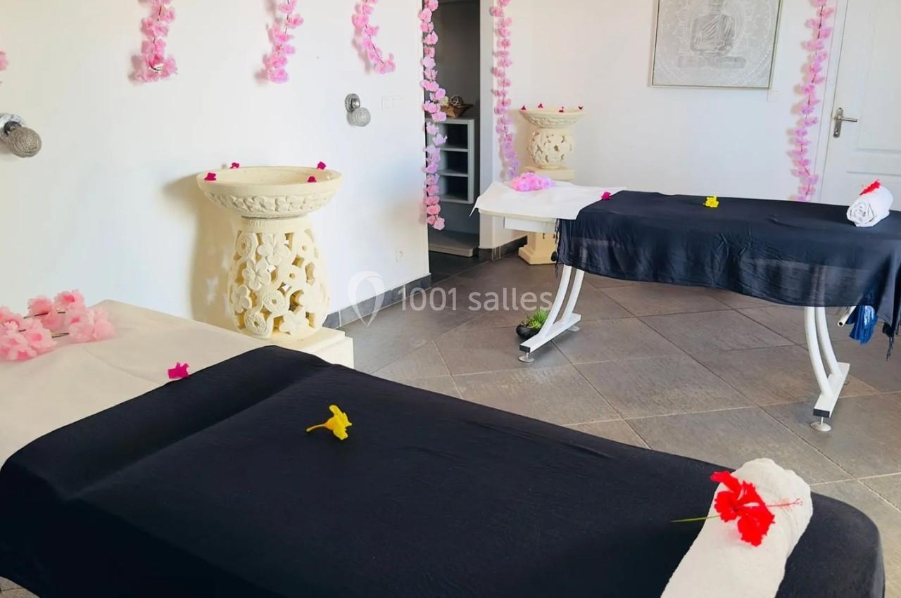Deux tables de massage couvertes de draps noirs dans une salle décorée de fleurs et de guirlandes roses.
