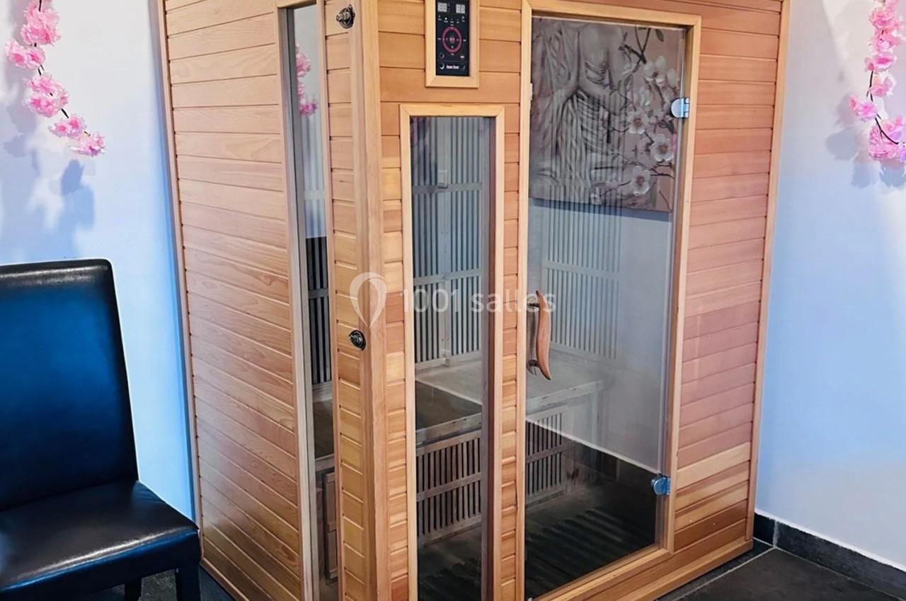 Cabine de sauna infrarouge en bois avec portes vitrées, entourée de décorations florales roses.