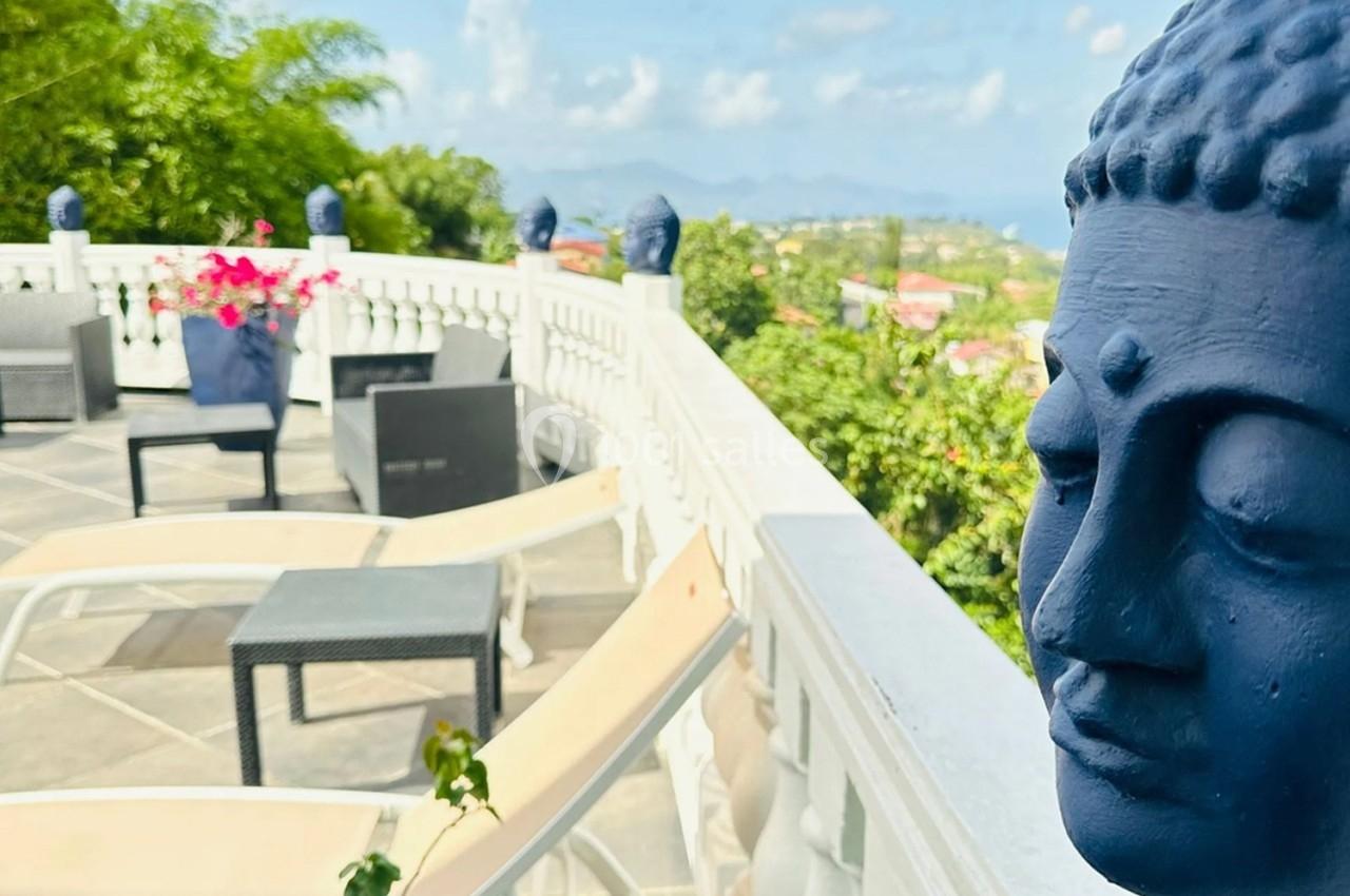 Statues de têtes de Bouddha bleues décorant une terrasse ensoleillée avec vue sur un paysage verdoyant.