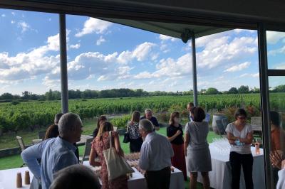 Un groupe de personnes échange autour d'un buffet en plein air, avec des serveurs et un paysage de vignoble en arrière-plan.